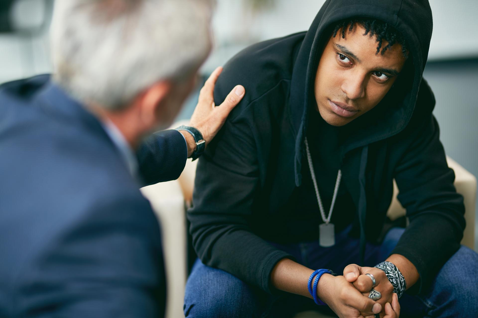 Mature psychotherapist encouraging black male adolescent during therapy at counselling center.