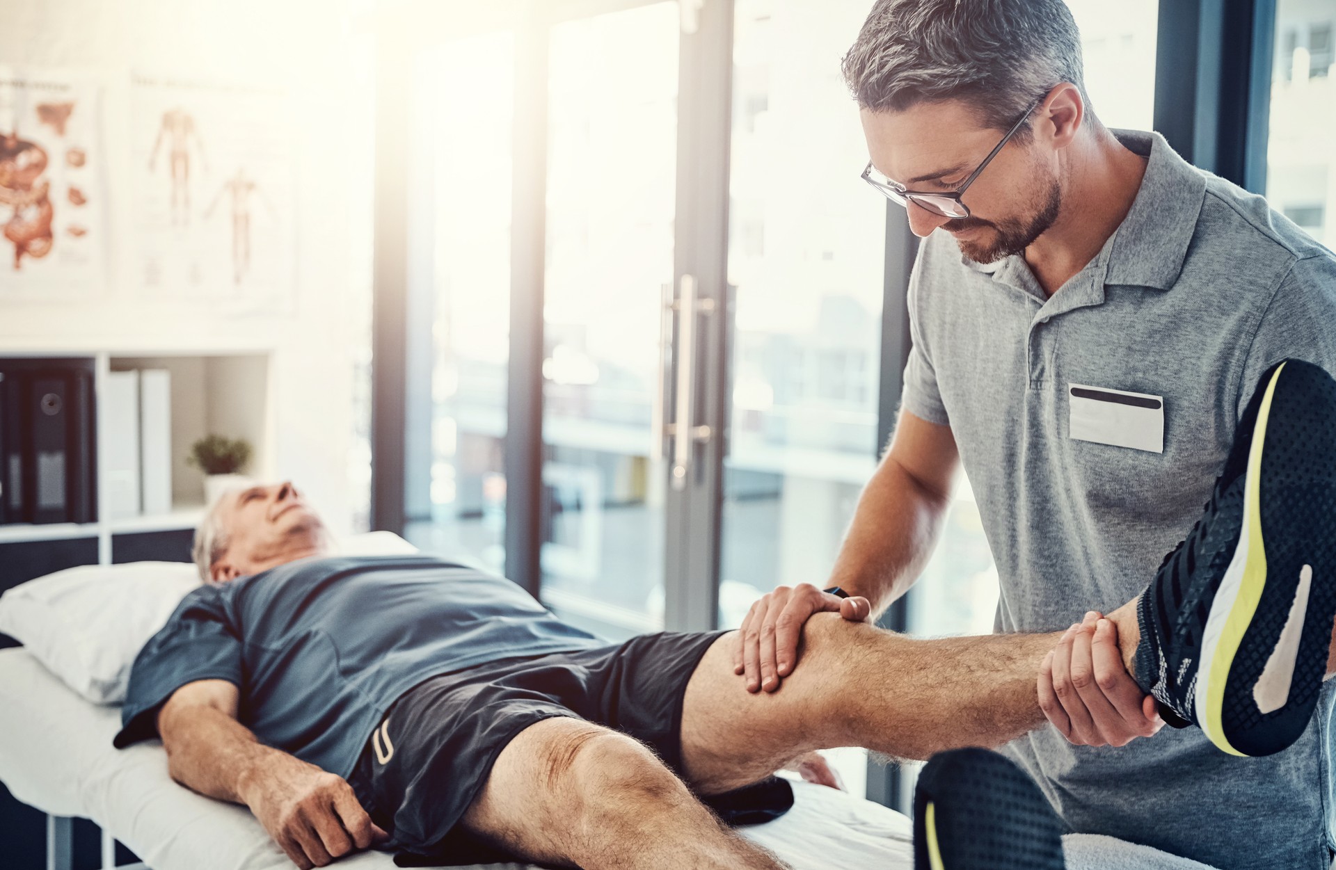 Physiotherapy, senior man and stretching leg for knee injury, medical and consultant with healthcare. Consultation, chiropractor and physical therapy with rehabilitation and care in doctor office