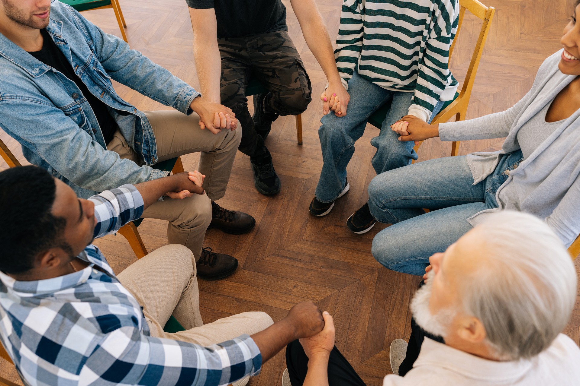 High-angle view of happy multi-ethnic and different ages people sitting in circle and holding hands. Psychotherapy training, business lecture or conference.